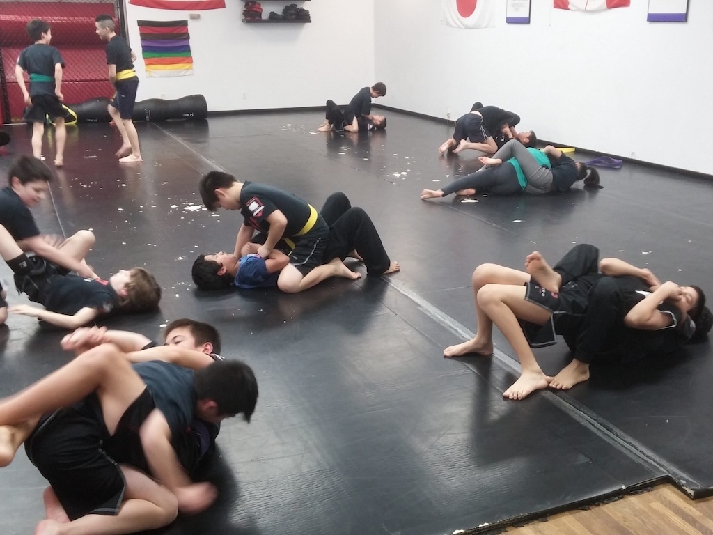 Kids practicing MMA grappling techniques on padded mats at a martial arts gym in Vancouver. The students wear colored belts and Posener’s Pankration uniforms, highlighting an engaging training session for MMA for kids in Vancouver or nearby areas
